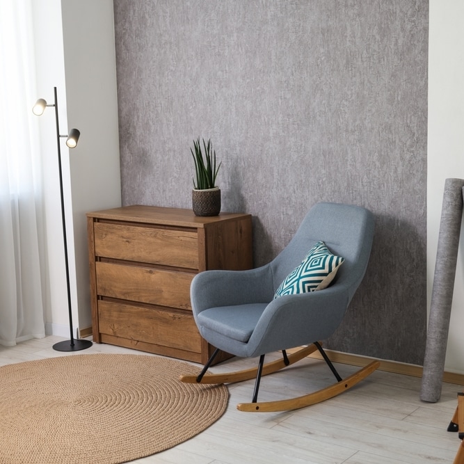 Fauteuil Rocking Chair Bleu et Commode en Bois Moderne Fauteuil à bascule bleu avec coussin géométrique, commode en bois et tapis rond en jute dans un salon moderne.
