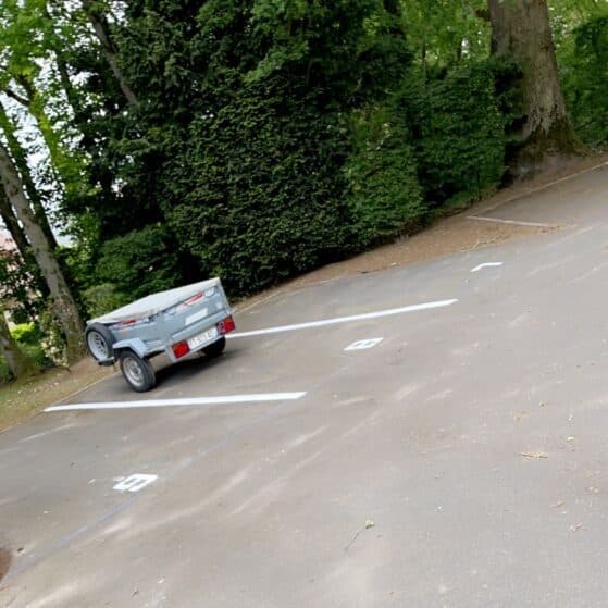 Remorque Grise Stationnée sur un Parking en Nature Petite remorque grise stationnée sur une place de parking numéro 9 entourée d'arbres.